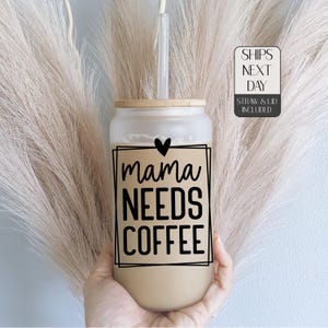 May include: A clear glass tumbler with a brown wooden lid and a black straw. The tumbler has a black and white graphic that says "mama needs coffee" with a heart above the word "mama".