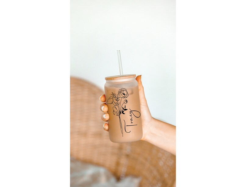May include: A clear glass tumbler with a brown lid and a black floral design. The tumbler has a straw and says "Tracy" on the side.