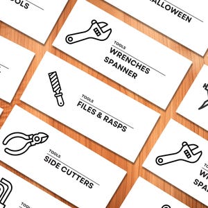 May include: White cards with black line drawings of tools, including wrenches, files, and side cutters. The cards have the word "TOOLS" and the tool names printed on them. The background is a light brown wood grain.