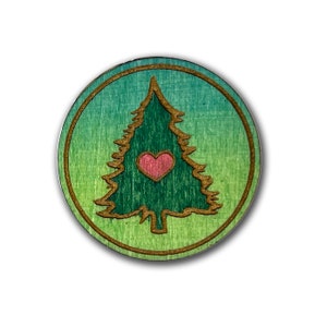 May include: A round wooden ornament with a green and blue gradient background. A brown outline of a pine tree with a pink heart in the center is in the middle of the ornament.