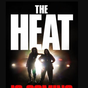 May include: Movie poster for the film "The Heat" featuring two women in silhouette standing in front of a car with headlights on. The text "The Heat is Coming" is in red and white.