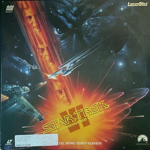 Op de afbeelding: Laserdisc-hoes voor Star Trek VI: The Undiscovered Country. De hoes toont een ruimtescène met de Enterprise, explosies en de gezichten van de personages. De titel is geel en rood, met het Paramount-logo.