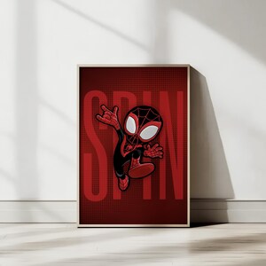 May include: Framed print with a cartoon superhero in a black and red suit. The word "SPIN" is in large red letters behind the character. The background is a dark red with a dotted pattern. The print is in a wooden frame.