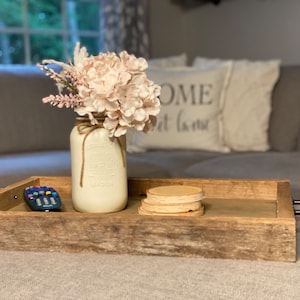 Könnte beinhalten: Ein Holztablett mit einem weiß lackierten Einmachglas, gefüllt mit rosa Blumen, einer Fernbedienung und drei Holz-Untersetzern. Das Tablett hat einen rustikalen Look und steht auf einer hellgrauen Oberfläche.