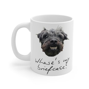 May include: White ceramic mug with a black dog's face and the text "Where's my briefcase?" in black cursive. The dog has a dark, shaggy coat and visible teeth, set against a white background.