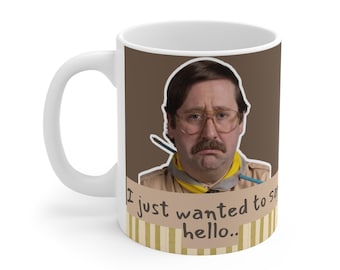 May include: A white ceramic mug featuring a graphic of a person with brown hair, glasses, and a mustache, wearing a tan shirt and yellow neckerchief. Below the figure, text on a tan background reads, I just wanted to say hello..