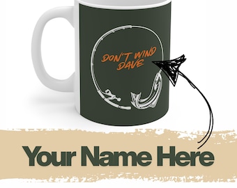 May include: White ceramic coffee mug with a dark green background. The mug features a white graphic of a fishing rod and a fish, with the text "DON'T WIND DAVE" in orange. The bottom of the mug has the text "Your Name Here".