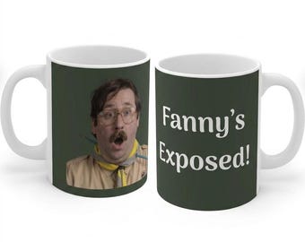 May include: Two white ceramic mugs with a dark green background. One mug features a photographic print of a person with glasses, a mustache, and a tan uniform with a yellow neckerchief. The other mug displays the white text Fanny's Exposed!