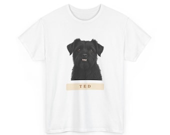 May include: A white short-sleeved t-shirt featuring a centered graphic of a black dog with shaggy fur and a visible snout. Below the dog, a light tan horizontal rectangular banner contains the text TED in dark brown capital letters.