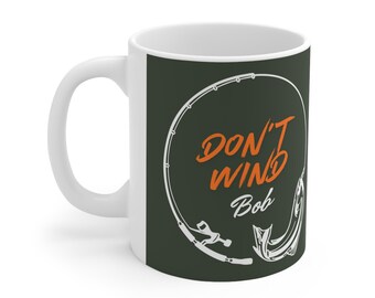 May include: White ceramic mug with a green background and a white fishing rod design. The text "Don't Win Bob" is written in orange on the mug.