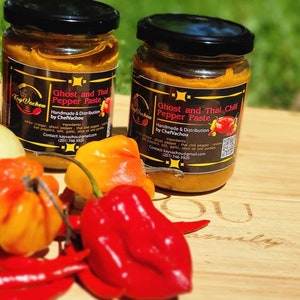 May include: Two glass jars of Ghost and Thai Pepper Paste, handmade and distributed by ChefVachou. The jars are labeled with the ingredients, contact information, and a QR code. The jars are surrounded by red and orange chili peppers.