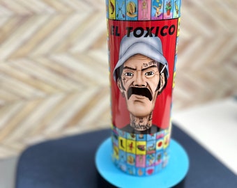 May include: A stainless steel tumbler with a colorful design featuring a cartoon character with a mustache and the text "EL TOXICO". The tumbler is on a blue base with the text "ANICK CREATIONS" printed on it.