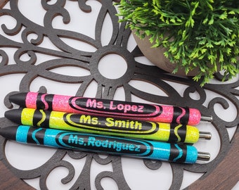 Può includere: Tre penne glitter colorate con tappi neri. Le penne sono etichettate "Ms. Lopez", "Ms. Smith" e "Ms. Rodriguez".
