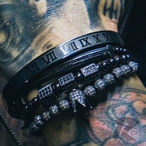 May include: A set of four black bracelets, one with Roman numeral markings, and three with black beads and silver accents.