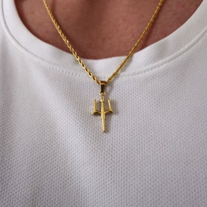 May include: A gold chain necklace with a gold trident pendant.