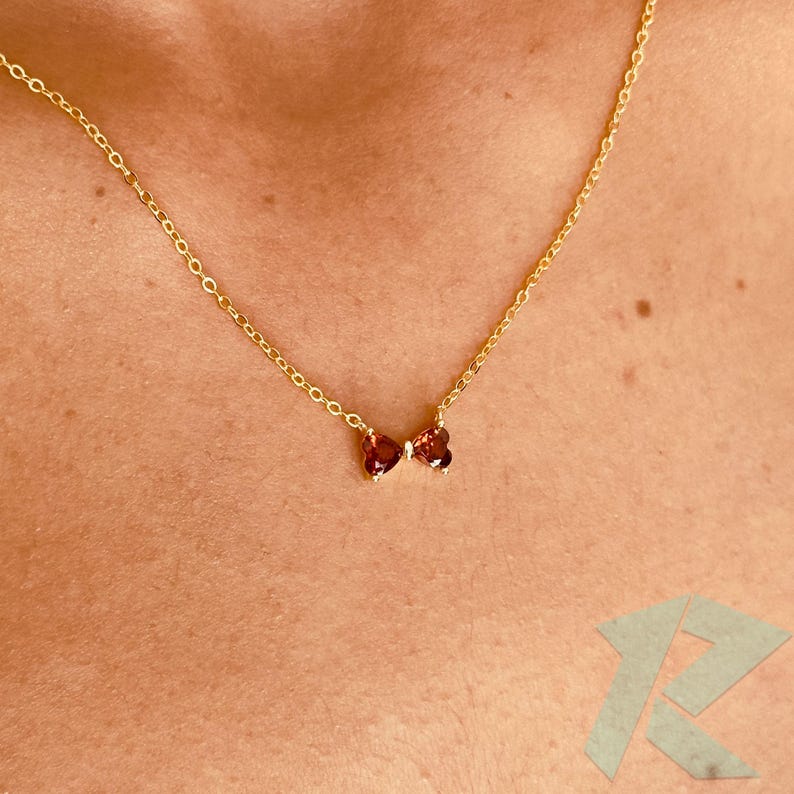 May include: A gold necklace with a butterfly pendant. The pendant is made of two reddish-brown gemstones, with a small, clear stone in the centre. The chain is a fine, linked design. The necklace is worn around the neck.