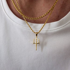 Op de afbeelding: Een gouden ketting met een gouden drietand hanger. De ketting is gelaagd met twee kettingen.