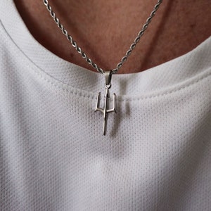May include: A silver chain necklace with a trident pendant. The trident is a three-pronged spear with a pointed tip.