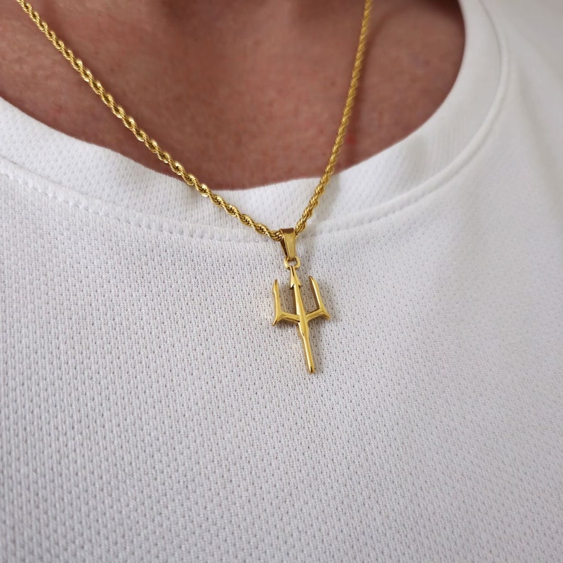 May include: A gold chain necklace with a trident pendant. The chain is a rope style and the pendant is a simple design.
