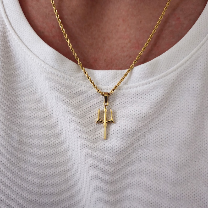 May include: A gold chain necklace with a trident pendant. The chain is a rope style and the pendant is a simple design.