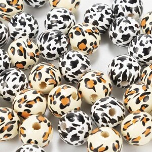 May include: A collection of round wooden beads with a leopard print design in shades of white, black, and orange.
