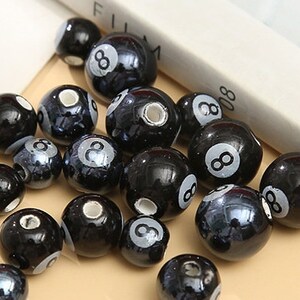 Könnte beinhalten: Eine Sammlung schwarzer und weißer Keramikperlen mit der Zahl acht darauf gedruckt. Die Perlen sind rund und haben eine glänzende Oberfläche.