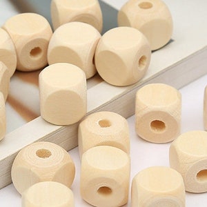 May include: A collection of 16 natural wooden beads, each with a square shape and a hole in the center. The beads are arranged on a white surface.