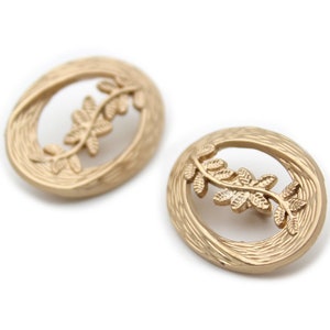 May include: A pair of gold oval-shaped earrings with a textured surface and a delicate leaf design.