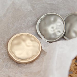 Könnte beinhalten: Nahaufnahme von drei metallischen, runden Dekorationsgegenständen. Einer ist goldfarben, die anderen beiden silbern. Die Objekte haben eine strukturierte, organische Form und sind auf einer hellen Oberfläche angeordnet, was auf ein Bastel- oder Schmuckthema hindeutet.