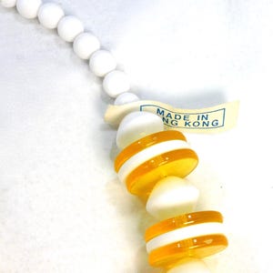May include: A necklace with white, round beads and alternating orange and white striped beads. A tag reads "MADE IN HONG KONG". The necklace is on a white background.