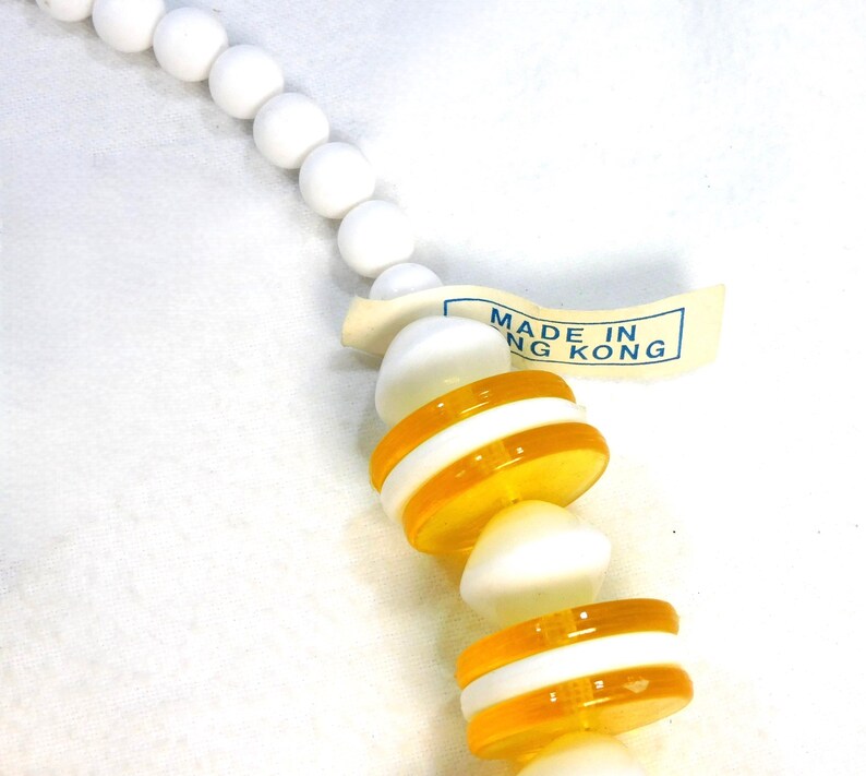 May include: A necklace with white, round beads and alternating orange and white striped beads. A tag reads "MADE IN HONG KONG". The necklace is on a white background.