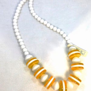 May include: A white beaded necklace with alternating sections of white and orange disc-shaped beads. The necklace has a tag that reads "MADE IN HONG KONG". The necklace is a vintage accessory.