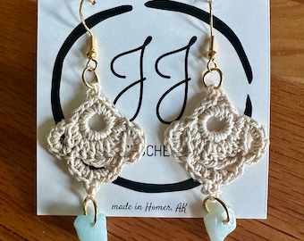 May include: Crocheted earrings with a light beige color and a light blue stone dangle. The earrings are on a white card with the text "JJ Crochet" and "made in Homer, AK".