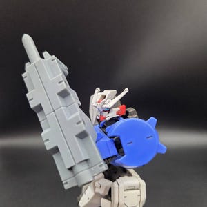 Op de afbeelding: Een plastic robotactiefiguur met een wit, blauw en grijs kleurenschema. Het figuur heeft een witte kop met rode accenten, een blauw schouderstuk en houdt een groot, rechthoekig grijs wapen vast in de rechterhand.