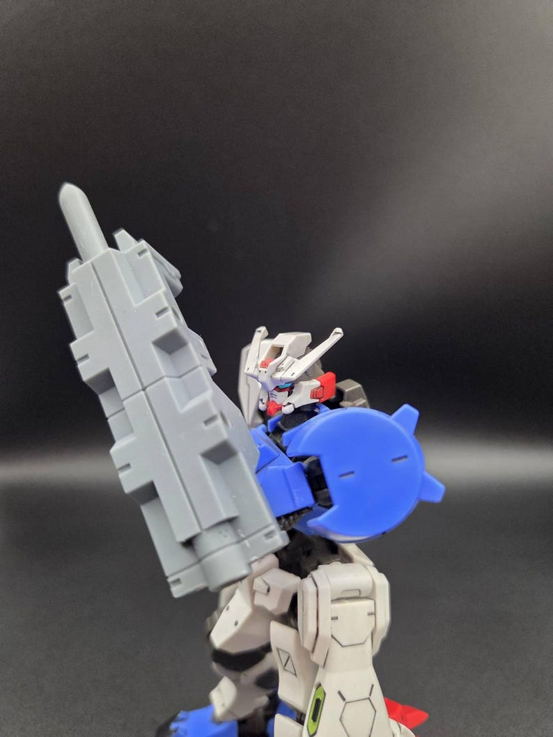Op de afbeelding: Een plastic robotactiefiguur met een wit, blauw en grijs kleurenschema. Het figuur heeft een witte kop met rode accenten, een blauw schouderstuk en houdt een groot, rechthoekig grijs wapen vast in de rechterhand.