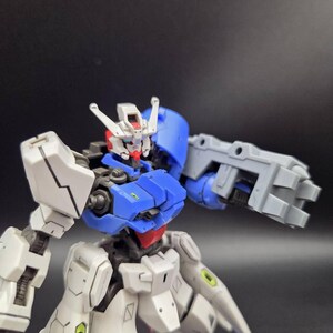Op de afbeelding: Een plastic robotactiefiguur met een wit, blauw en grijs kleurenschema. Het figuur heeft een gedetailleerd hoofd met een rode kin, een blauwe borstplaat en een grote grijze mechanische armbevestiging. Het ontwerp bevat kleine groene accenten.