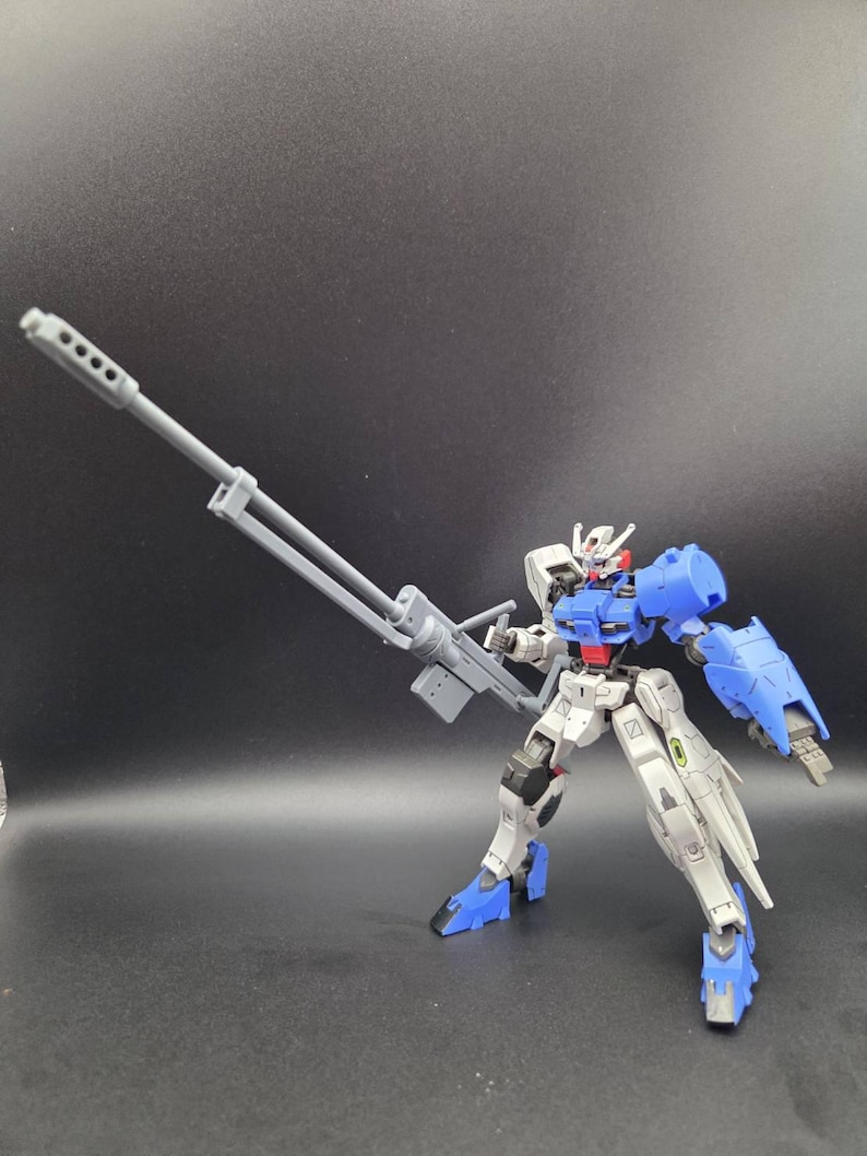 Op de afbeelding: Een beweegbaar robotactiefiguur met een wit, blauw en rood kleurenschema. Het figuur is uitgerust met een groot, grijs geweer met een lange loop in de rechterhand. Het heeft een gedetailleerd hoofd, beweegbare ledematen en blauwe pantserplaten op de schouders, voeten en de linkeronderarm.