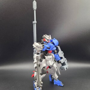 Op de afbeelding: Een beweegbaar robotactiefiguur met een blauw, wit en grijs kleurenschema. Het figuur is uitgerust met een lang grijs kanon op de rug, een grijs geweer in de hand en een groot grijs schild bevestigd aan de linkerarm.