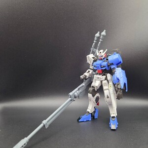 Op de afbeelding: Een wit, blauw en grijs robotactiefiguur dat rechtop staat. Het figuur heeft een gedetailleerd mechanisch ontwerp met een lang grijs geweer in de rechterhand, twee grijze kanonnen op de rug en blauwe schouderpantserplaten.