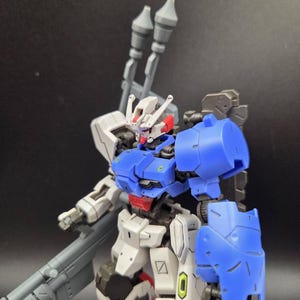 Op de afbeelding: Een plastic robotfiguur met een kleurenschema van wit, blauw en grijs. Het figuur heeft een gedetailleerd hoofd met rode accenten, een blauw borststuk en een groot grijs wapen op de rug. Het staat met beweegbare ledematen.