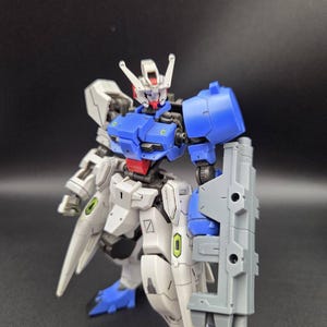 Op de afbeelding: Een beweegbaar robotactiefiguur met een wit, blauw en grijs kleurenschema met rode accenten op het hoofd en de taille. Het figuur heeft een gedetailleerd mechanisch ontwerp met beweegbare gewrichten, een schild op de linkerarm en puntige beenpantser.