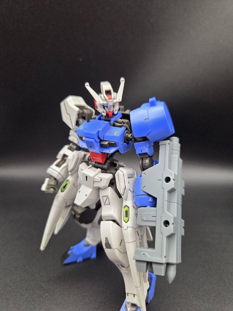 Op de afbeelding: Een beweegbaar robotactiefiguur met een wit, blauw en grijs kleurenschema met rode accenten op het hoofd en de taille. Het figuur heeft een gedetailleerd mechanisch ontwerp met beweegbare gewrichten, een schild op de linkerarm en puntige beenpantser.