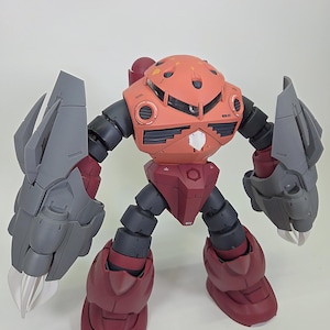 Puede incluir: Modelo detallado de robot en tonos rojos y grises. Presenta una cabeza y torso redondeados, y grandes manos en forma de garra. El robot está posado sobre un fondo liso. El texto "#emodelworkshop" es visible.