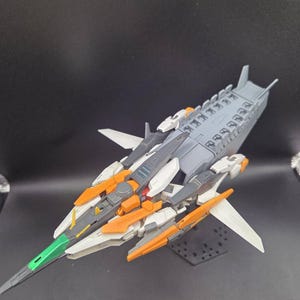 Op de afbeelding: Een plastic ruimteschipmodel met een grijs, wit en oranje kleurenschema en een groene, puntige neus. Het vaartuig heeft meerdere vleugelachtige structuren, een gedetailleerde mechanische romp en de tekst #emodelworkshop onderaan.