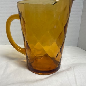 May include: A amber glass pitcher with a diamond pattern. The pitcher has a handle and a wide mouth.