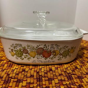 May include: White casserole dish with a glass lid. The dish has a floral pattern with green leaves, yellow lemons, red peppers, and the text "La Marjolaine".
