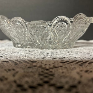 May include: A clear glass bowl with a scalloped edge and a decorative pattern of small, raised dots. The bowl is sitting on a white lace tablecloth.