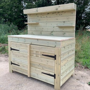 May include: A wooden outdoor work bench with a backsplash and two doors. The bench has a light wood finish and black hinges.