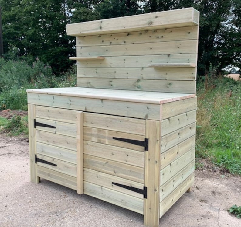 May include: A wooden outdoor work bench with a backsplash and two doors. The bench has a light wood finish and black hinges.
