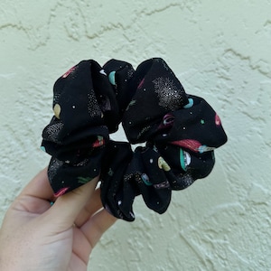 May include: A black scrunchie with a space-themed print featuring planets, stars, and comets.